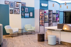 Un interior moderno con un mostrador de recepción, dos sillas, una mesa de centro, una estantería y una pared decorada con cuadros.