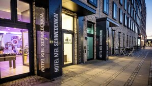 A hotel with large glass windows, a visible interior with a reception desk, and a brick facade. - Hotel Kiel-Schwedenkai (Kiel)