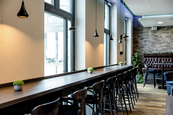 Un espace bar doté d’un long comptoir, de nombreuses chaises, de luminaires suspendus et d’un mur en briques en arrière-plan.