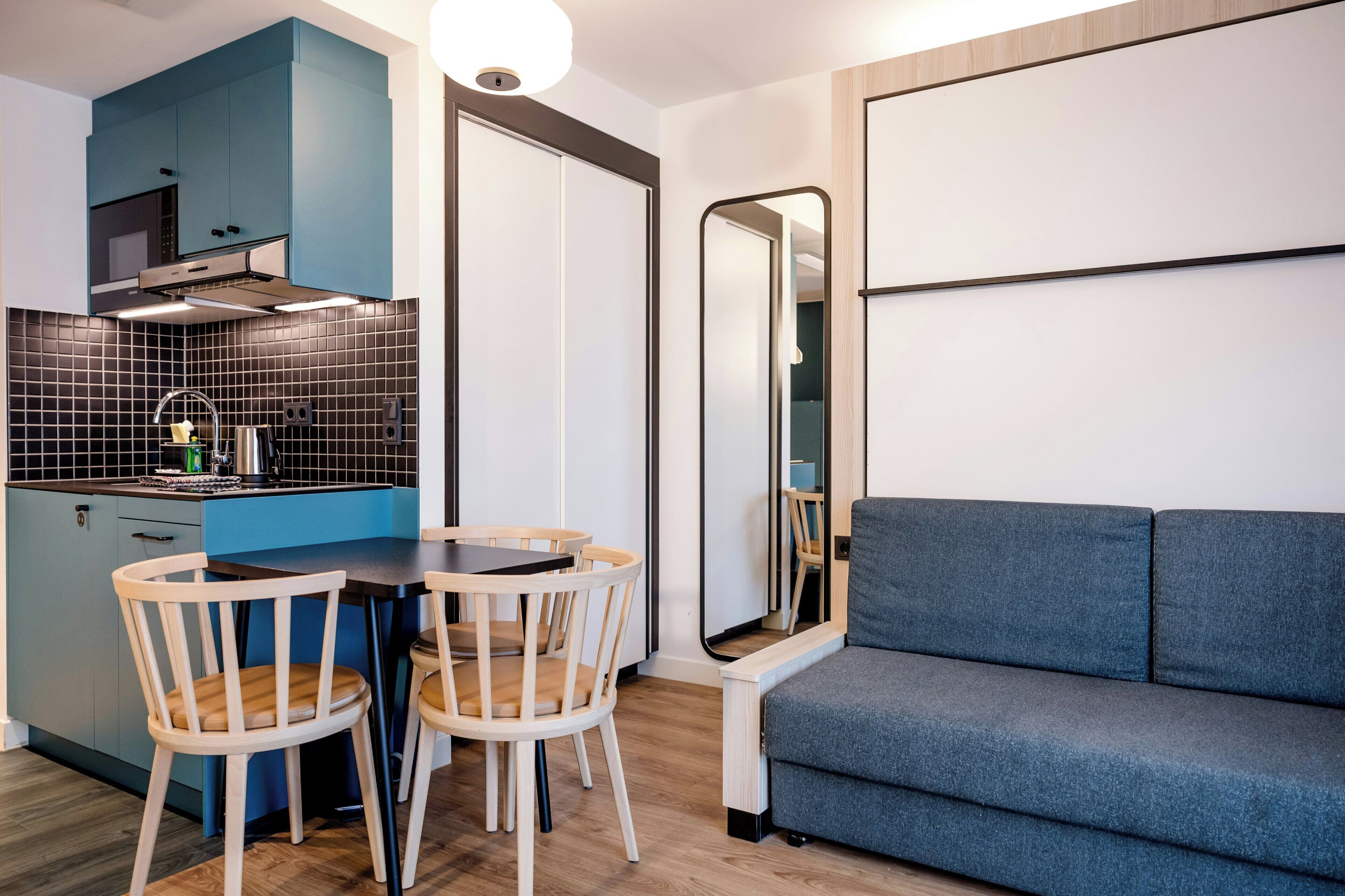 Un espacio habitable compacto con kitchenette, un área de comedor con dos sillas, un sofá y un espejo grande.