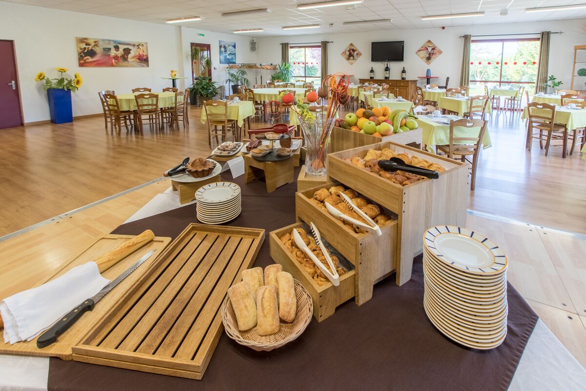 Uma área de refeições com várias mesas e cadeiras, um buffet com diversos pratos e uma televisão na parede.