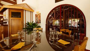 A dining table set for four with a glass top, surrounded by wooden chairs, and a wine rack in the background.