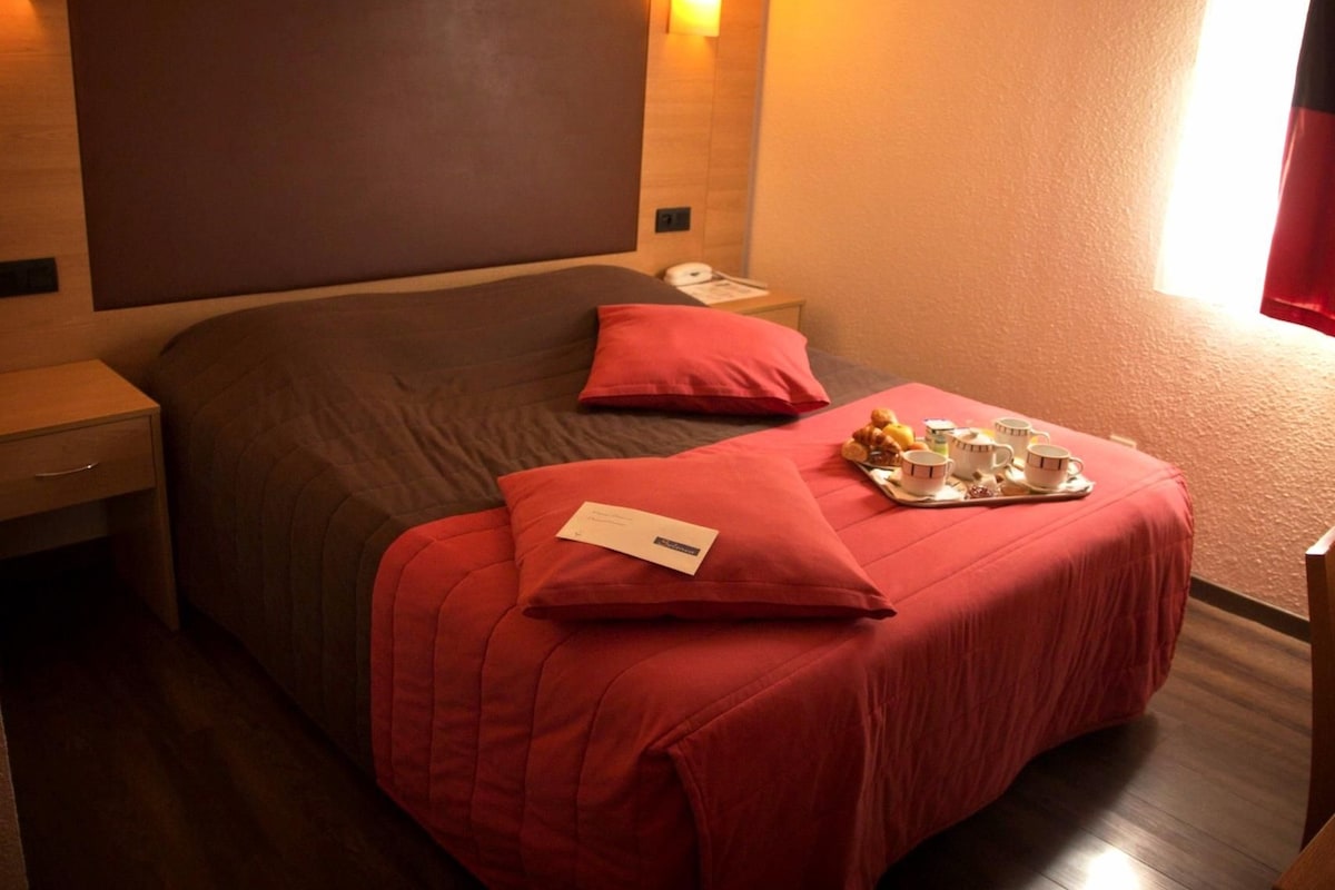 A hotel room with a large bed, a nightstand, a tray with breakfast items, and a red pillow.