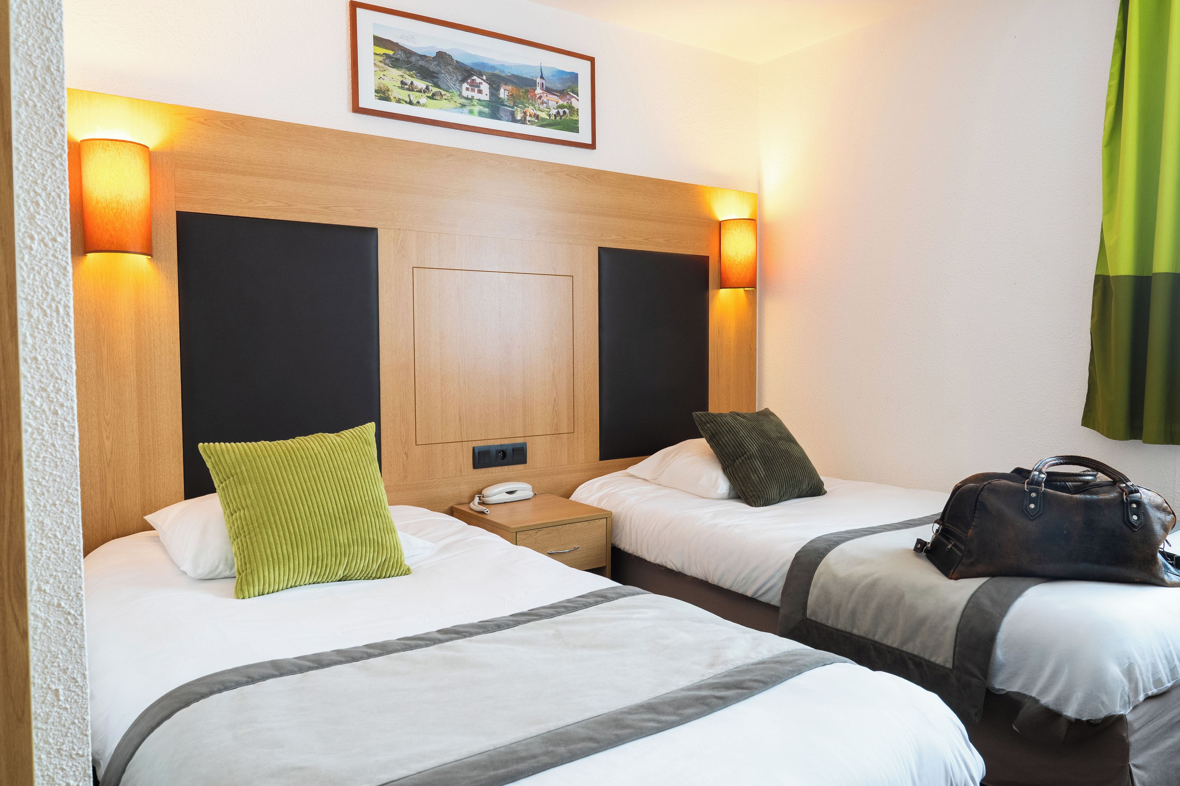 Ein Hotelzimmer mit zwei Betten, einem hölzernen Kopfteil, Nachttischlampen, einem Telefon und einer Handtasche auf dem Boden.
