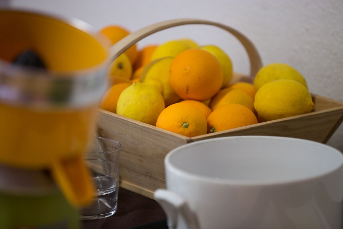 A wooden crate filled with oranges and lemons, a clear glass, and a white mug on a table.