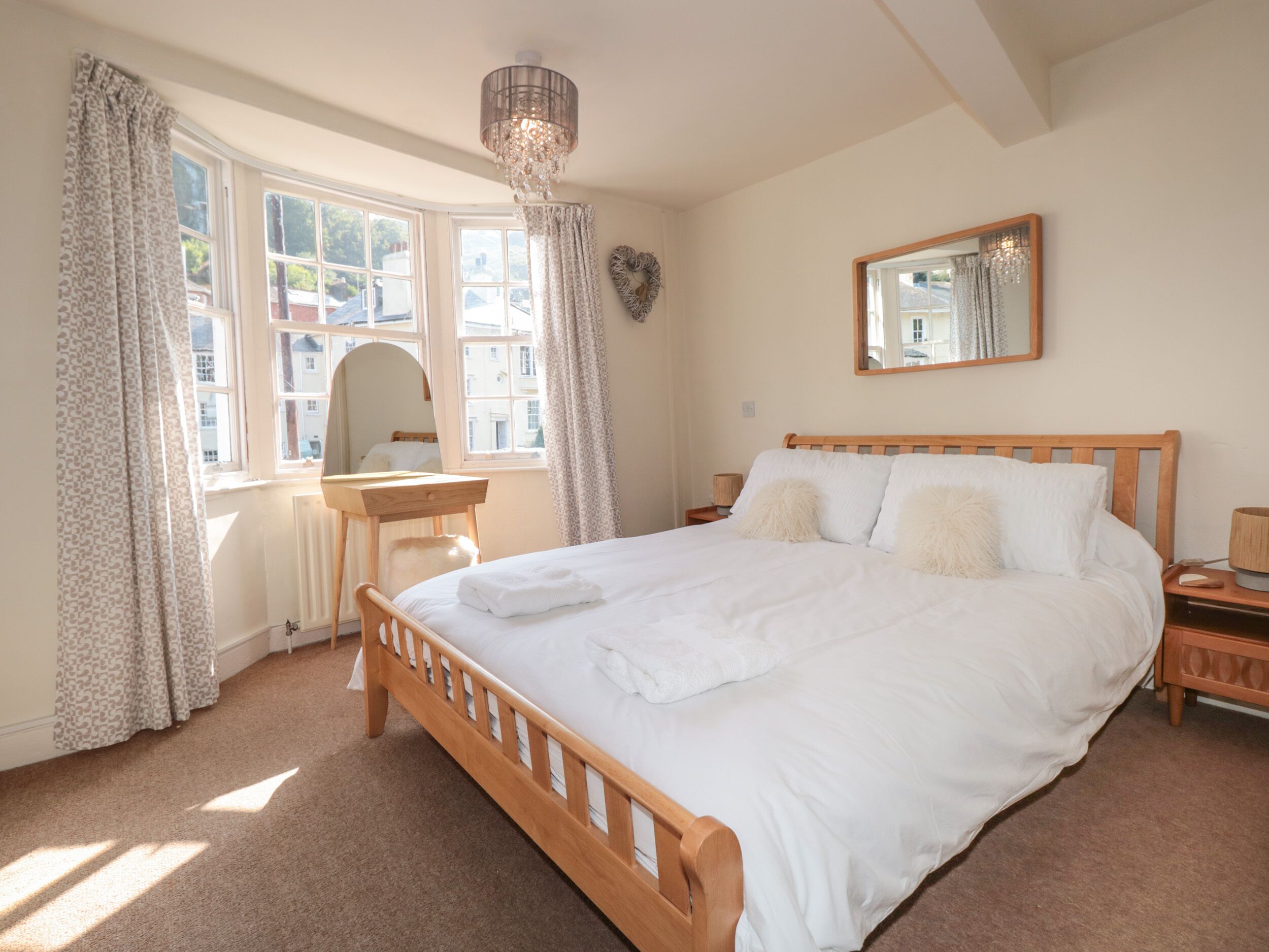 A bedroom with a wooden bed, a desk, a chair, a mirror, and a chandelier.