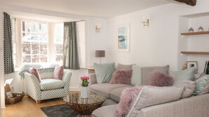 A living room with a sofa, armchair, and coffee table. There is a window with curtains, a lamp, and a framed picture on the wall. - Nookie Cottage (Dartmouth)