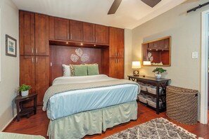 A bedroom with a large bed, wooden cabinets, a desk, and a mirror. - Beachfront 1BR ocean view condo with pool and hot tub summer deals (Kihei)