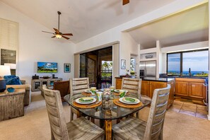 A dining area with a glass table, wooden chairs, and a view of the ocean through large windows. - Ocean Views and Exquisite Getaway Wailea Ekahi 53D! (Wailea)