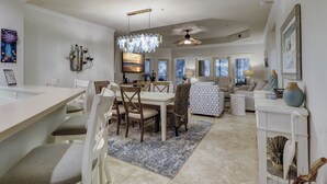 A spacious living room with a dining area, large windows, and a chandelier. - 8126 Wendover Dunes - Palmetto Dunes Oceanside Community (Hilton Head Island)