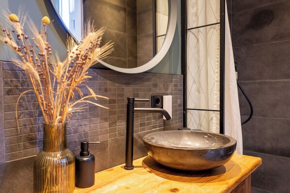 A bathroom with a round vessel sink, a modern faucet, a vase with dried plants, and a mirror.