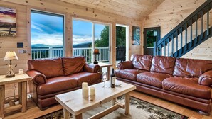 L’intérieur chaleureux d’un chalet avec deux canapés en cuir, une table en bois et de grandes fenêtres offrant une vue panoramique.