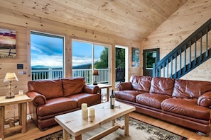A cozy cabin interior with two leather couches, a wooden table, and large windows offering a scenic view.