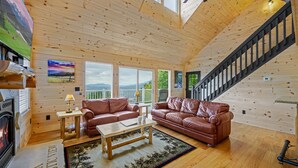 L’intérieur chaleureux d’un chalet avec des murs en bois, une cheminée, des canapés en cuir, une table à manger et un escalier.