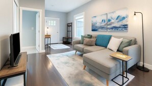 A modern living room with a grey sofa, a flat-screen TV, and a coffee table. There are abstract paintings on the wall and a floor lamp. - Fremont Bungalow with Backyard View Seattle (Seattle)
