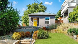 A modern two-story house with a yellow door, a small front yard with a stone staircase, and a grassy area. - Fremont Bungalow with Backyard View Seattle (Seattle)