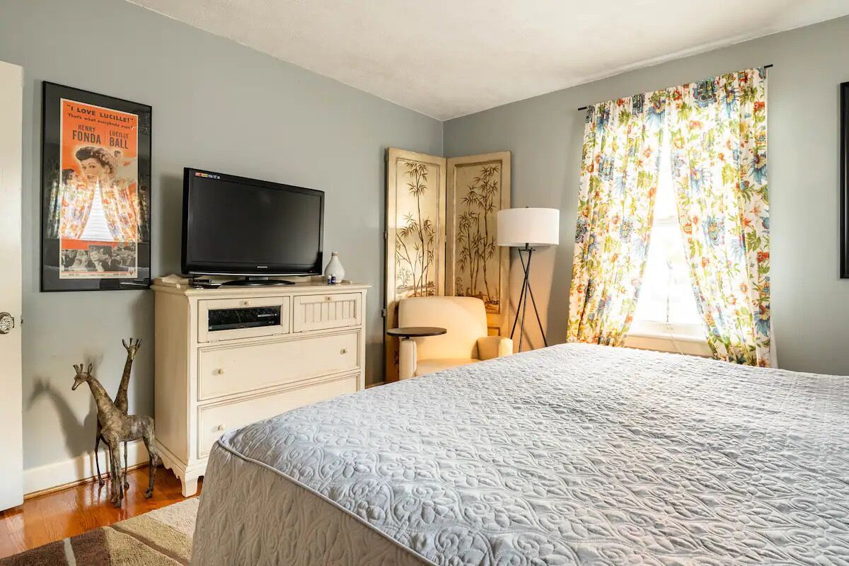 Une chambre à coucher avec un lit, une commode, un téléviseur, une lampe et une affiche accrochée au mur.