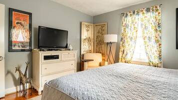 Une chambre à coucher avec un lit, une commode, un téléviseur, une lampe et une affiche accrochée au mur.