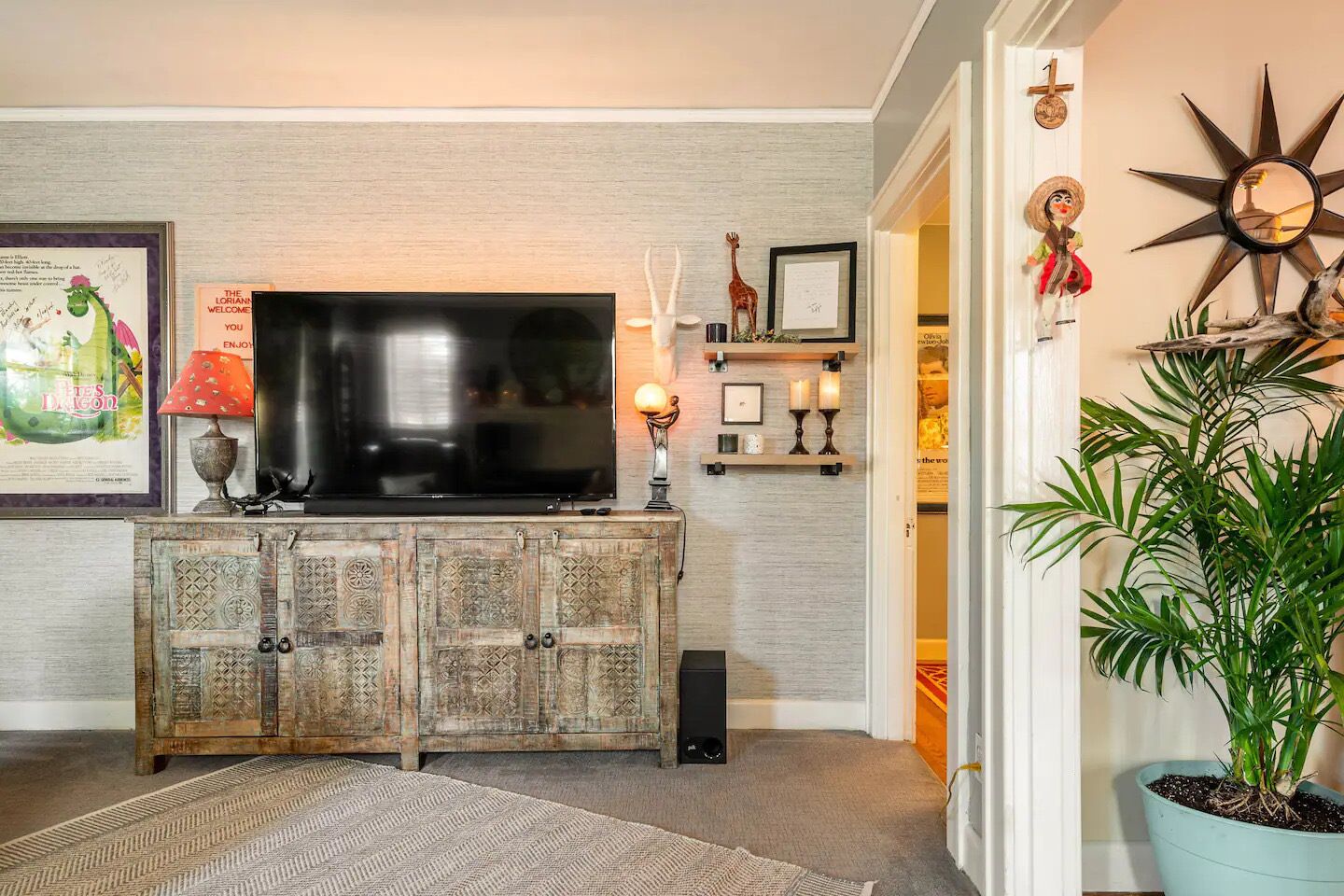 A living room with a television on a wooden cabinet, a potted plant, and a wall with decorative items.