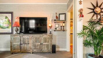 A living room with a television on a wooden cabinet, a potted plant, and a wall with decorative items.