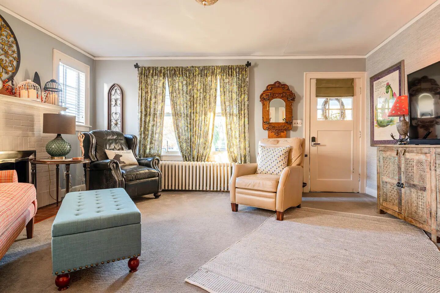 A living room with a fireplace, a sofa, a chair, and a large window with curtains.