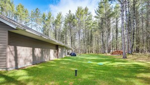 A house with a covered porch, a well-maintained lawn, and a stack of firewood in the yard. - Pet-Friendly Woodruff Cabin Near Lakes (Woodruff)