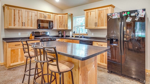 A modern kitchen with wooden cabinets, a stainless steel refrigerator, and a central island with bar stools. - Pet-Friendly Woodruff Cabin Near Lakes (Woodruff)