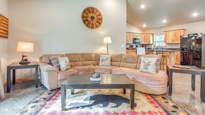 A living room with a sectional sofa, a coffee table, and a rug with a deer design. There is a wooden clock on the wall and a lamp on a side table. - Pet-Friendly Woodruff Cabin Near Lakes (Woodruff)