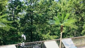 A deck with two lounge chairs and a small table, surrounded by lush greenery.