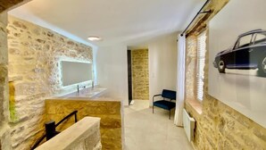 A modern room with stone walls, a large mirror, a sink, a chair, and a car poster. - Grand Luxe SENSATION Suite with private Jacuzzi (Martignargues)