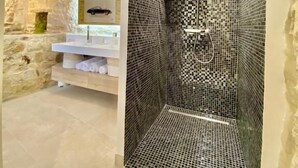 A bathroom with a stone wall, a tiled shower, and a white sink. - Grand Luxe SENSATION Suite with private Jacuzzi (Martignargues)