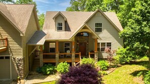 Une maison à deux étages, avec des fondations en pierre, un porche à l’avant et un garage.