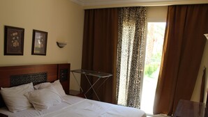 A hotel room with a bed, a small table, a wall-mounted lamp, and curtains. - One-Bedroom Apartment with a Garden in Sahl Hasheesh (Hurghada)