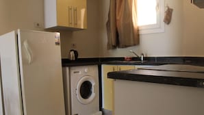 A compact kitchen with a refrigerator, washing machine, and a small countertop. - One-Bedroom Apartment with a Garden in Sahl Hasheesh (Hurghada)