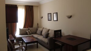 A living room with a sofa, two chairs, a coffee table, and a TV. - One-Bedroom Apartment with a Garden in Sahl Hasheesh (Hurghada)