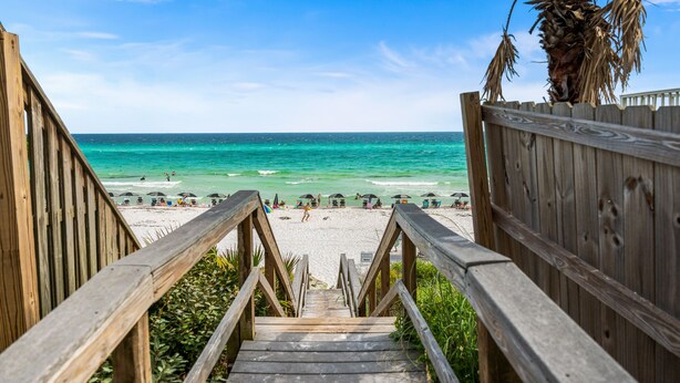A wooden staircase leading to a beach with umbrellas and a palm tree. - Sea You Soon 1 Bedroom Condo by RedAwning (Santa Rosa Beach)