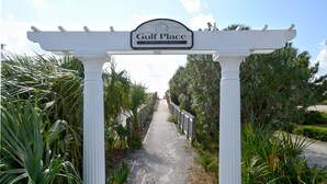 A pathway leading to a white archway with a sign reading "Gulf Place at Santa Rosa Beach." - Sea You Soon 1 Bedroom Condo by RedAwning (Santa Rosa Beach)