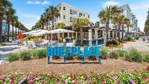 A hotel entrance with a sign reading "GULERPLACE," outdoor seating, palm trees, and a clear sky. - Sea You Soon 1 Bedroom Condo by RedAwning (Santa Rosa Beach)