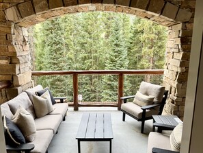 A stone-walled balcony with a wooden railing, furnished with a sofa, armchairs, and a small table.