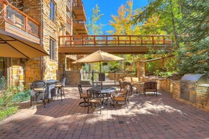 Une terrasse extérieure avec des murs en pierre, un espace salon abrité et un barbecue.