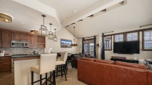 A spacious kitchen with a bar area, a large brown leather sofa, and a flat-screen TV mounted on the wall. - Cozens Pointe B-301 3 Bedroom Condo by RedAwning (Fraser)