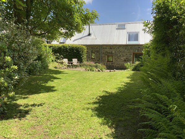 A stone building with a metal roof, surrounded by lush greenery and a grassy yard.