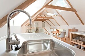 A modern kitchen with a stainless steel sink, wooden beams, and a dining area with a table and chairs.