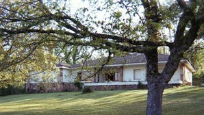Une maison avec un toit en pente, des fondations en pierre et une pelouse bien entretenue.