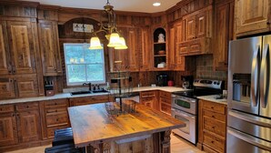 Una cocina con armarios de madera, una isla central con taburetes, un refrigerador de acero inoxidable y una lámpara colgante.