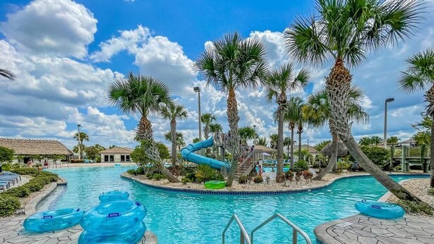 Ein Swimmingpool mit Wasserrutsche, umgeben von Palmen und einer Stegterrasse.