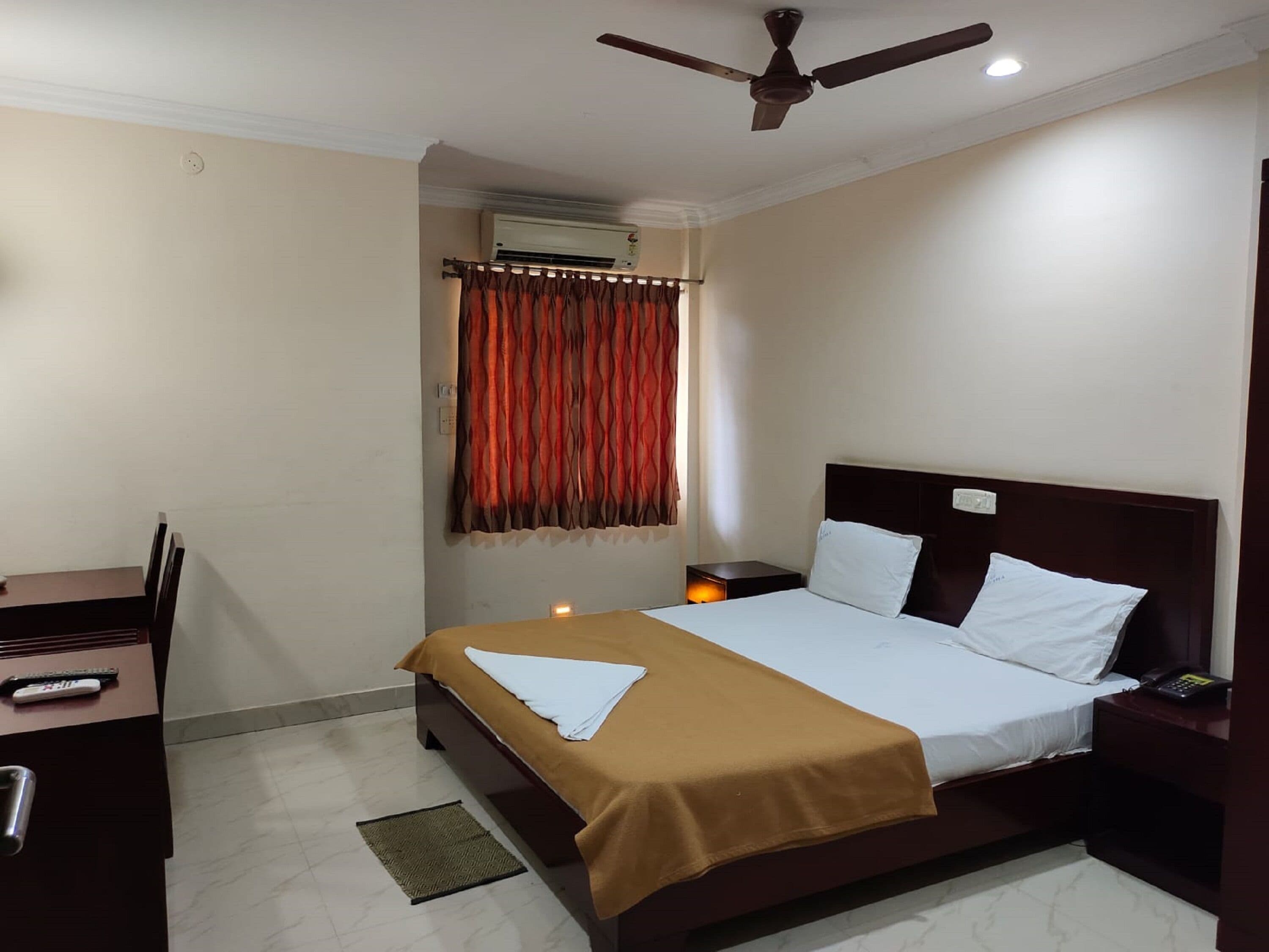 A hotel room with a bed, a desk, a chair, a ceiling fan, and an air conditioning unit.