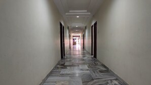 A hallway with marble flooring and doors on both sides, leading to a bright room at the end. - Hotel Geetha International (Thoothukudi)