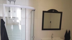 Un baño con cabina de ducha de vidrio, lavamanos con espejo y un cubo de basura.