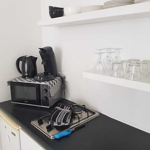 A kitchenette with a microwave, coffee maker, and gas stove. There are glassware on a shelf above.